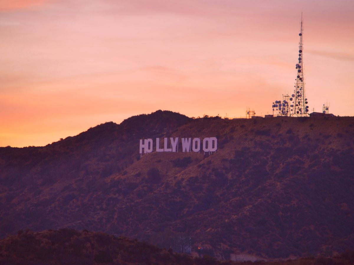 A scenic view of the famous Hollywood sign on a hill at sunset, with a tall radio tower visible to the right.