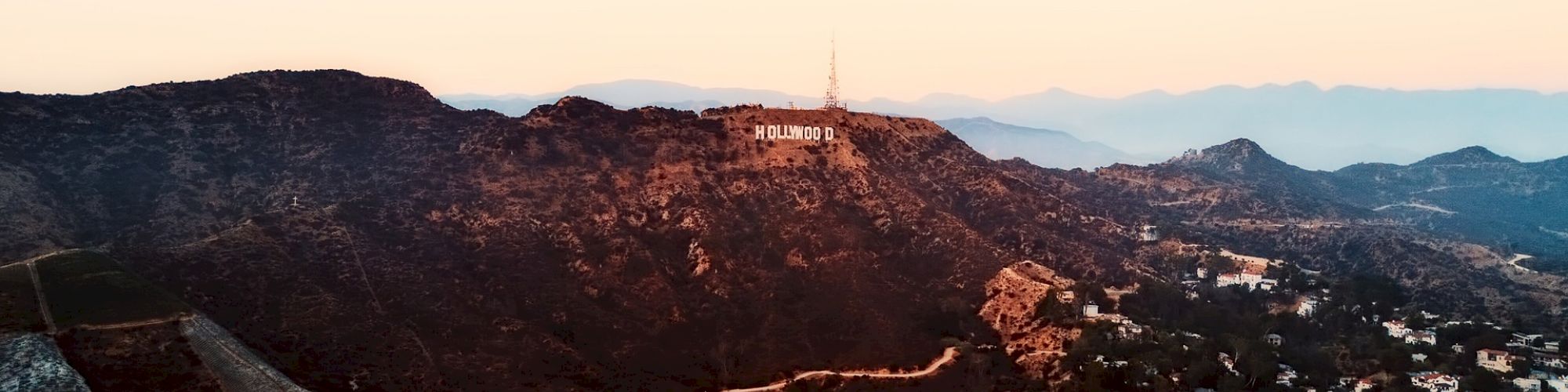 This image depicts the Hollywood Hills with the famous Hollywood sign, surrounded by homes, winding roads, and mountain terrain.