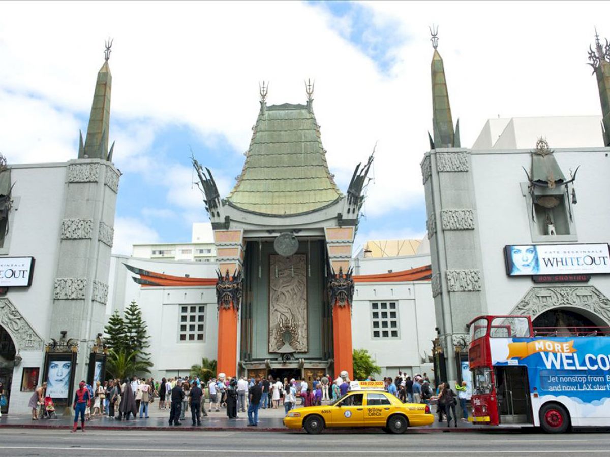 An iconic theater with tourists outside, a yellow taxi, and a sightseeing bus in front. Ending the sentence.