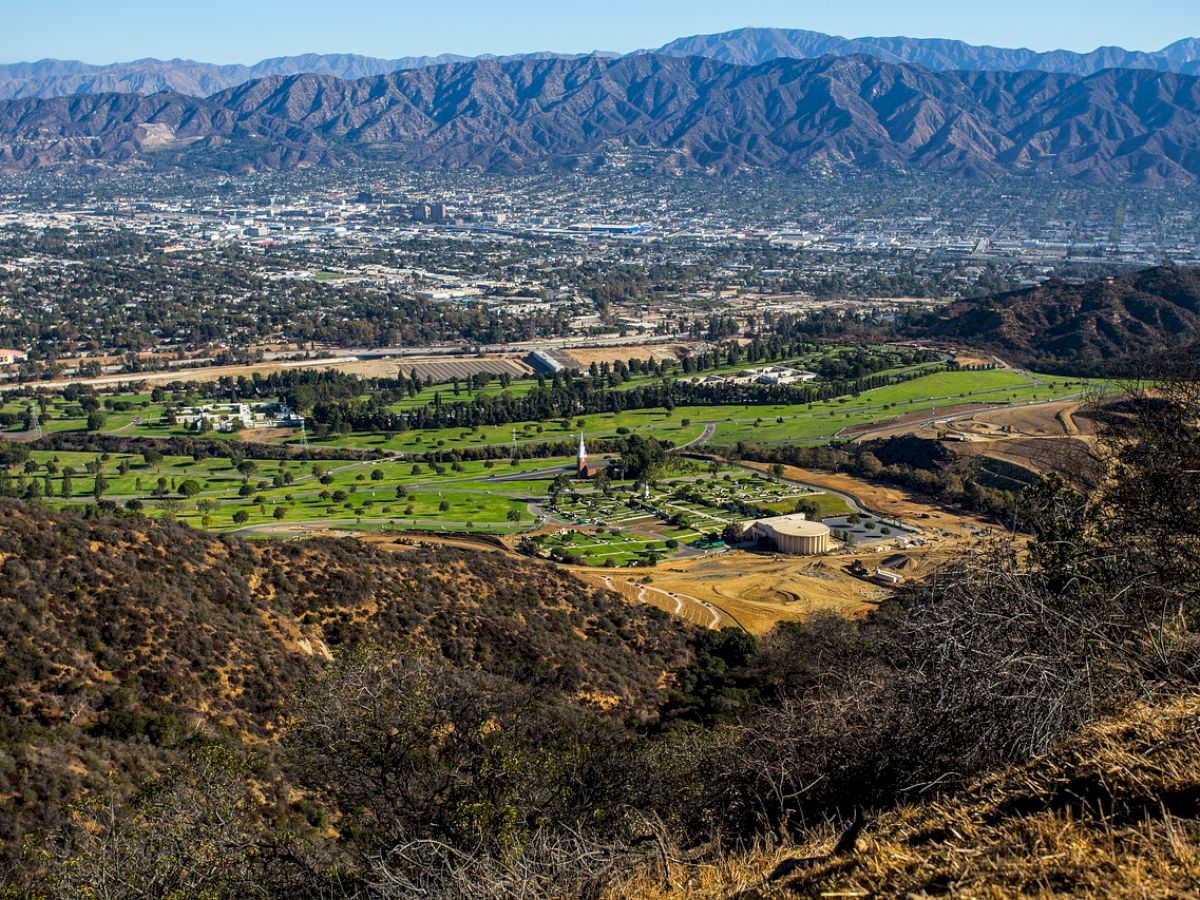 A panoramic view of a golf course surrounded by hills, with a city and mountains visible in the background.