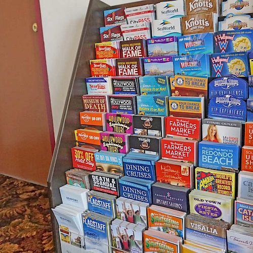 The image shows a display rack filled with various travel brochures and maps for tourist destinations and attractions in a hallway.