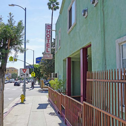 A sidewalk along a green building with a hotel sign in the distance, and palm trees in the background under a clear sky, ending the sentence.