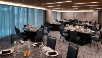 The image shows an elegantly set dining room with round tables, chairs, glassware, and table settings, ready for an event or banquet.