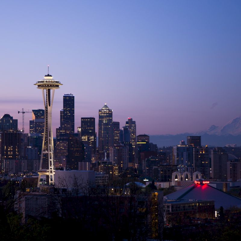 The image shows a nighttime cityscape featuring the Seattle skyline with the Space Needle prominently visible and Mount Rainier in the background.