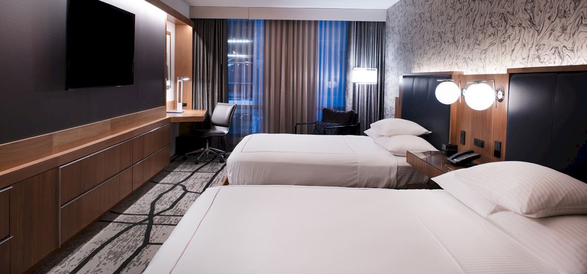A hotel room with two beds, a desk, and a TV on the wall.