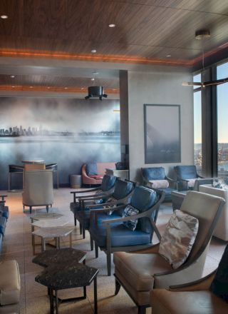 A modern lounge with leather chairs, a cityscape mural, and large windows offering a scenic view of the waterfront and Ferris wheel in the distance.