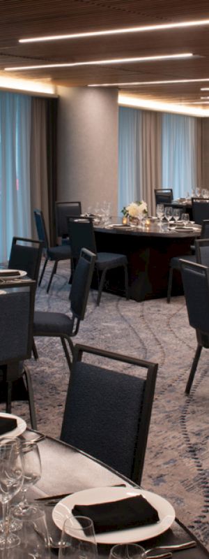 A banquet hall set up with round tables covered with black tablecloths, elegant place settings, and flower centerpieces under modern lighting.