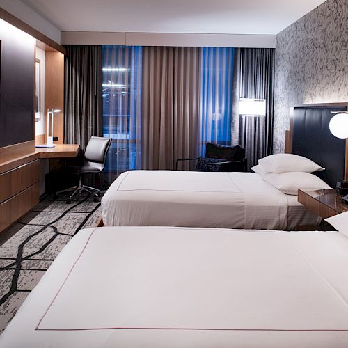 A modern hotel room with two beds, a large TV, a desk, and contemporary decor, including a patterned wall and geometric carpet.