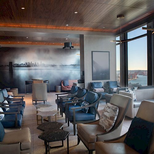 A modern lounge area with comfortable seating and a scenic view of a city skyline and waterfront through large windows, elegantly designed.