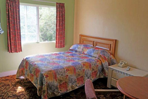 A hotel room with a bed, nightstand, desk, and window.
