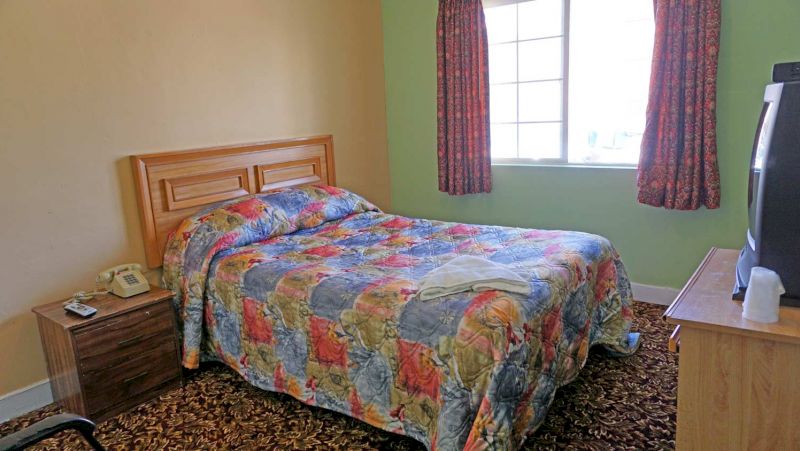 A hotel room with a bed, nightstand, TV, and window.