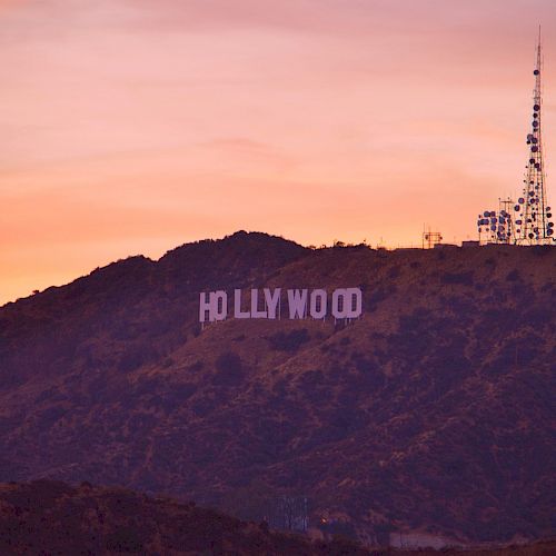 The image shows the iconic Hollywood Sign on a hillside during sunset, with a large antenna tower also visible on the right side of the image.