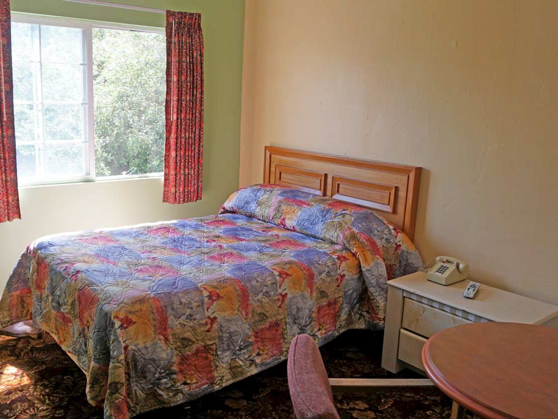 A hotel room with a bed, nightstand, telephone, and window.
