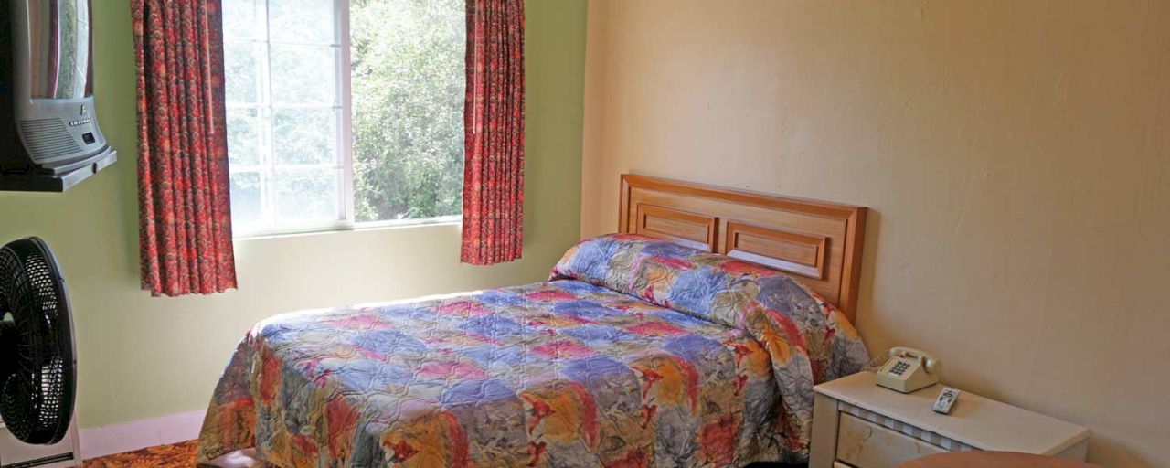A hotel room with a bed, nightstand, TV, and fan.